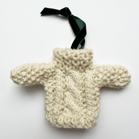 Mini Aran handknit Ireland Christmas ornament made from soft natural wool with traditional cable stitches, shown laid flat with a velvet ribbon attached.