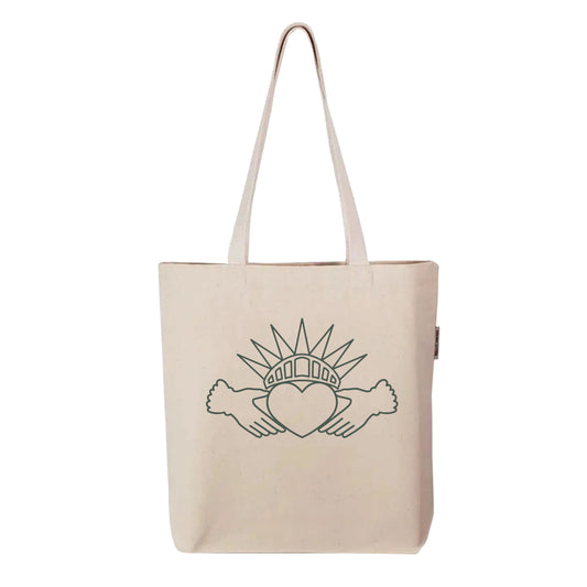 Held Here tote bag by FYRNE — organic cotton canvas tote featuring a symbolic design combining the Irish Claddagh and Statue of Liberty crown, printed in green on natural fabric.