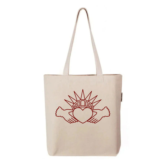 Held Here tote bag by FYRNE — organic cotton canvas tote featuring a symbolic design combining the Irish Claddagh and Statue of Liberty crown, printed in red on natural fabric.