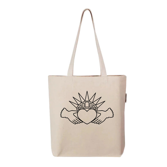 Held Here tote bag by FYRNE — organic cotton canvas tote featuring a symbolic design combining the Irish Claddagh and Statue of Liberty crown, printed in black on natural fabric.